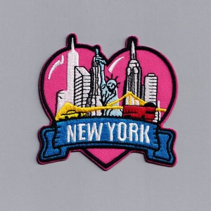 Puede incluir: Parche bordado con forma de corazón rosa con el horizonte de Nueva York. El diseño incluye la Estatua de la Libertad, rascacielos y un puente, con el texto "NEW YORK" en una pancarta azul.