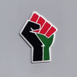 May include: A black, green, and red embroidered patch depicting a raised fist. The fist is a symbol of solidarity and resistance.