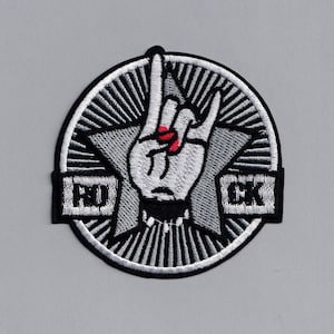 May include: A black and white embroidered patch featuring a star and a hand making the rock and roll sign. The words "ROCK" are on the patch.
