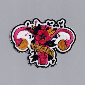 May include: Embroidered patch featuring a pink and white uterus with a red flower and green leaves. The text "My Body My Choice" is embroidered in yellow on a black ribbon.
