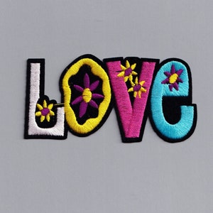 May include: A colorful embroidered patch with the word "LOVE" in a retro style. The letters are outlined in black and filled with different colors, including yellow, pink, and blue. Each letter has small embroidered flowers in various colors.