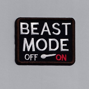 Könnte beinhalten: Schwarzer und brauner gestickter Aufnäher mit weißem Text, der "BEAST MODE OFF ON" lautet, mit einem weißen Kippschalter in der Mitte.