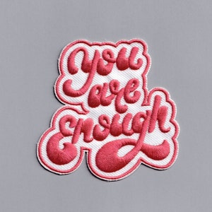May include: Pink embroidered patch with the text "You are enough" on a white background.