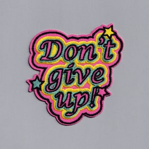 Könnte beinhalten: Rosa, gelber und grüner gestickter Aufnäher mit dem Text "Don't give up!" in schwarzen Buchstaben.