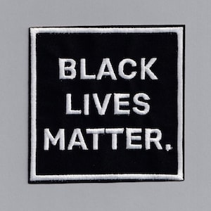 May include: Black Lives Matter embroidered patch on a black background with white stitching. The patch is square shaped and has a white border.