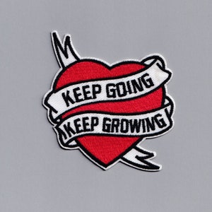 Può includere: Cuore rosso ricamato con uno striscione bianco che recita "Keep Going Keep Growing".