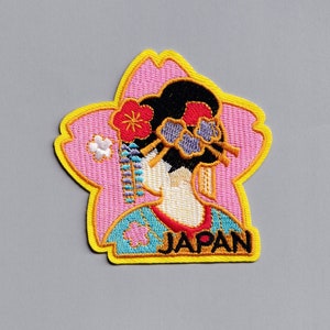 Peut inclure: Patch brodé représentant une femme en kimono japonais traditionnel avec un motif de cerisier rose et le mot "JAPON" en lettres jaunes.
