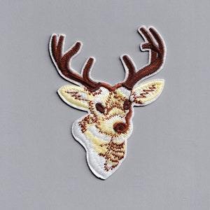 Puede incluir: Parche bordado para planchar de una cabeza de ciervo marrón y blanca con cuernos.
