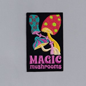 Könnte beinhalten: Ein schwarzer gestickter Aufnäher mit drei bunten Pilzen und dem Text "MAGIC mushrooms" in Rosa.