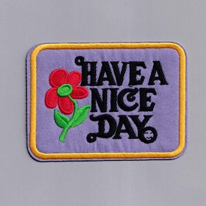 May include: Purple embroidered patch with a yellow border. The patch features a red flower with green leaves and the text "HAVE A NICE DAY" in black.