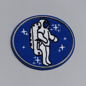 May include: A blue and white embroidered patch featuring an astronaut in a spacesuit with a star background.