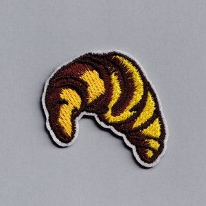 以下が含まれることがあります： 茶色と黄色の刺繍でできたクロワッサンのパッチ