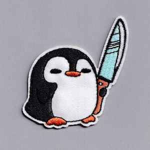 Könnte beinhalten: Ein gestickter Pinguin, der ein blaues Messer hält. Der Pinguin ist schwarz-weiß mit orangefarbenen Füßen und einem weißen Bauch.