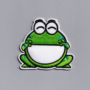 May include: Green and white embroidered frog patch with a smiling face. The frog is sitting with its legs crossed and has a white belly.