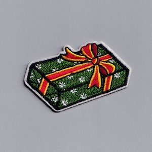 May include: A green gift box with a red and yellow bow. The box is decorated with white snowflakes.