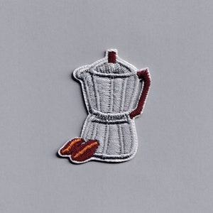 May include: White embroidered iron coffee pot with a brown handle and a brown coffee bean design.