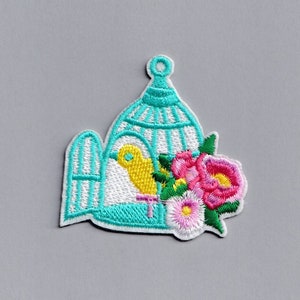 May include: A turquoise birdcage with a yellow bird inside and pink and white flowers on the side.