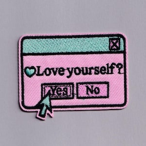 Peut inclure: Un écusson brodé rectangulaire avec une barre supérieure bleu clair ornée d'une icône X et une zone principale rose. Le texte indique Love yourself? avec un cœur, et deux boutons Yes et No. Un curseur bleu clair pointe sur le bouton Yes.