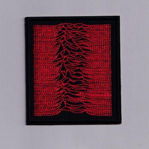 May include: A square, embroidered patch with a black border. The patch features a red background with a black, stylized graphic of a mountain range or sound wave. The design is centered within the patch.