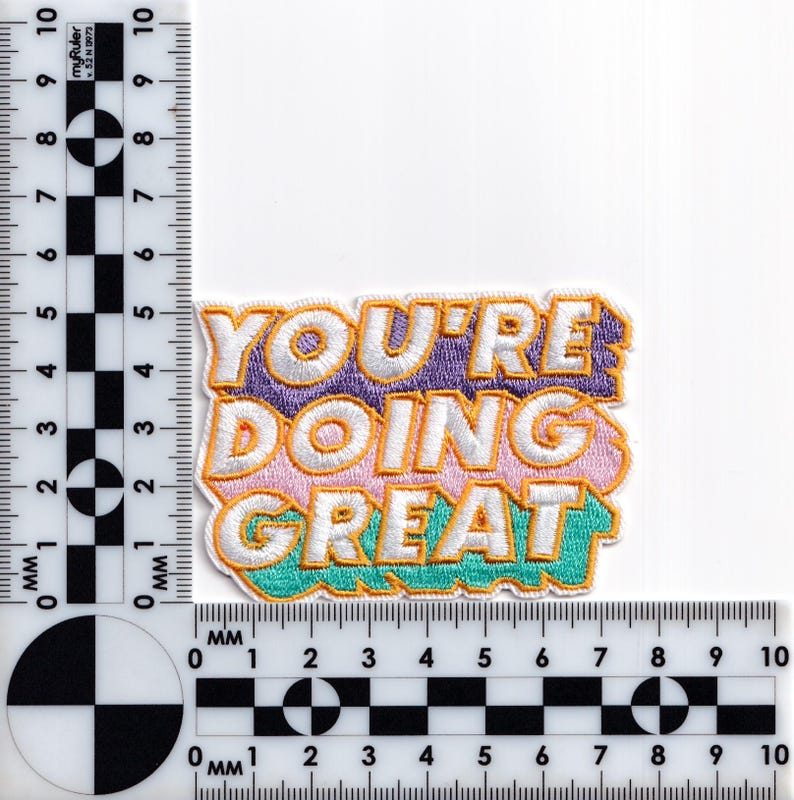 May include: An embroidered iron-on patch with the text "YOU'RE DOING GREAT" in a colorful, layered font style. The words are outlined in yellow and the background is a gradient of purple, pink, and teal.
