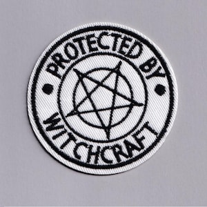 Peut inclure: Écusson rond blanc avec texte brodé noir et pentagramme. Les mots « PROTECTED BY WITCHCRAFT » sont brodés sur le bord. Deux points noirs de chaque côté du texte complètent le design.