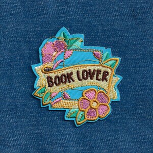 May include: A blue and gold embroidered patch with a floral design and the text "BOOK LOVER".