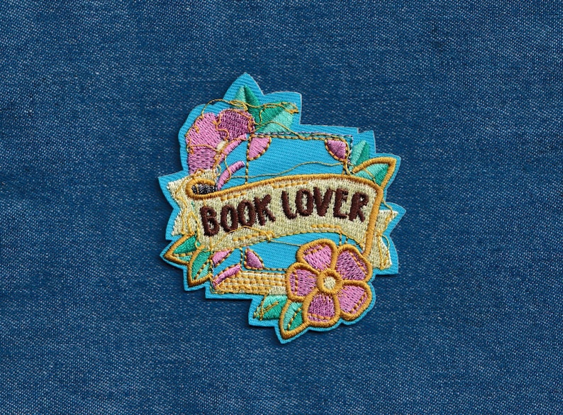May include: A blue and gold embroidered patch with a floral design and the text "BOOK LOVER".