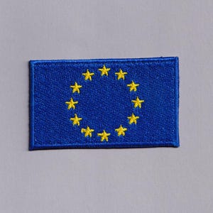 May include: A rectangular blue patch with a circle of twelve yellow stars, the symbol of the European Union. The stars are arranged in a circle on a blue background. The patch has a stitched border.