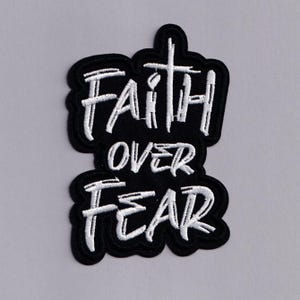 May include: Black embroidered patch with the words "FAITH OVER FEAR" in white, stylized lettering. The patch has a black border and a cross design incorporated into the word "FAITH".
