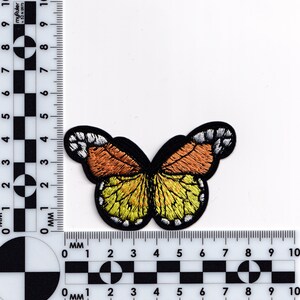 May include: A yellow and orange embroidered butterfly patch with black outlines. The butterfly has white accents on the wings.