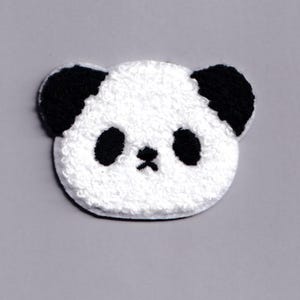 Pode incluir: Um patch de rosto de panda branco e preto. O patch apresenta uma textura branca fofa para o rosto, com orelhas, olhos e um pequeno nariz pretos. O patch de panda é um design fofo e caprichoso.