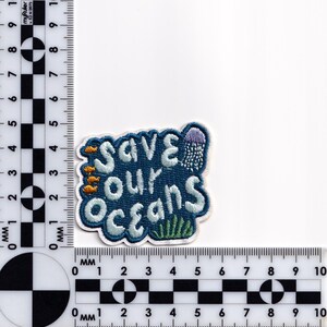 Pu&ograve; includere: Toppa ricamata con la scritta "Save Our Oceans" in bianco, bordata di azzurro chiaro, su sfondo blu scuro. La toppa presenta piccoli pesci, una medusa e alghe. La toppa misura circa 5 cm per 5 cm.