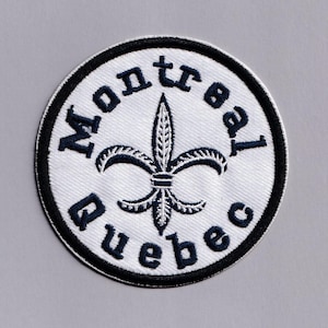 May include: A round, white embroidered patch with the words "Montreal Quebec" in navy blue lettering. A navy blue fleur-de-lis is centered on the patch. The patch has a black border.