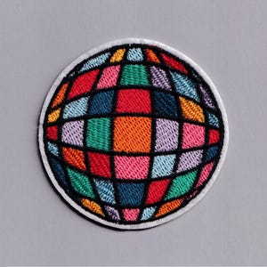 May include: A colorful, embroidered patch featuring a globe design. The globe is segmented into various shapes and filled with vibrant colors including red, orange, green, blue, and pink. The patch has a white border and is set against a gray background.