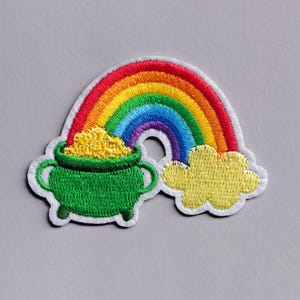 Può includere: Toppa ricamata raffigurante un arcobaleno sopra un vaso verde pieno di monete d'oro. Una nuvola gialla è accanto al vaso. La toppa ha un bordo bianco.