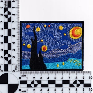 May include: Embroidered patch featuring a rendition of Vincent van Gogh's 'Starry Night' painting. The patch depicts a swirling night sky with a bright yellow moon and stars, a dark cypress tree, and a village in the distance. The colors are vibrant and the details are intricate.