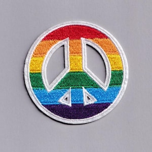 Może przedstawiać: Okrągła, haftowana naszywka z symbolem pokoju w kolorach tęczy: czerwonym, pomarańczowym, żółtym, zielonym, niebieskim i fioletowym. Symbol jest obrysowany na biało, z białą obwódką. Naszywka jest na szarym tle.
