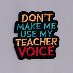 May include: Embroidered patch with the text "DON'T MAKE ME USE MY TEACHER VOICE". The text is in orange, teal, and red, outlined in black. A humorous accessory for teachers.