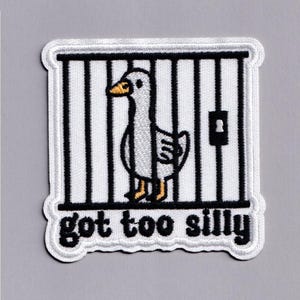 Op de afbeelding: Geborduurde patch met een cartoon gans in een kooi. De gans is grijs en wit met een gele snavel en poten. De kooi is zwart en wit, en de tekst "got too silly" staat eronder.