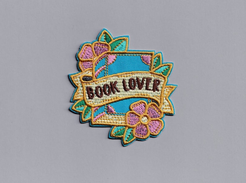 May include: A blue and gold embroidered patch with a book, flowers, and the text "BOOK LOVER".