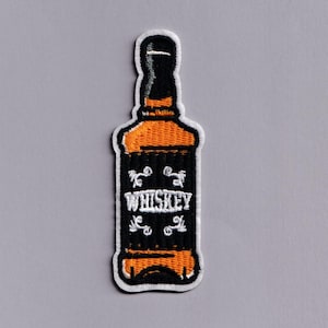 Könnte beinhalten: Gestickter Aufnäher in Form einer Whiskeyflasche. Der Aufnäher hat ein schwarzes Etikett mit dem Wort "WHISKEY" in weißer Schrift und dekorativen weißen Verzierungen. Die Flasche hat orange und schwarze Details mit einem weißen Rand.