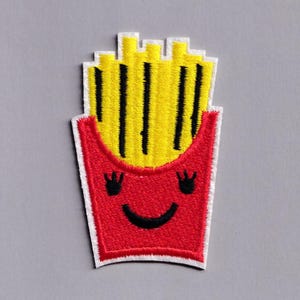May include: Embroidered patch featuring a smiling face on a red french fry container, with yellow fries and black vertical lines. The patch has a white border and is on a gray background.