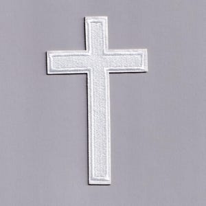May include: A white embroidered cross patch with a textured surface. The cross has a rectangular border around the arms and the top of the vertical beam. The patch is on a grey background.