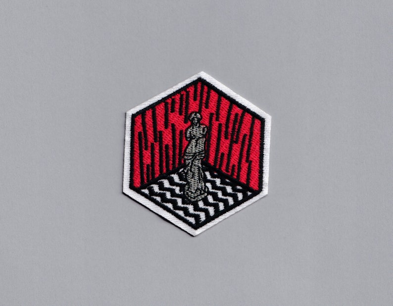 May include: A red and white embroidered patch with a black and white checkered pattern and a figure standing in the center. The patch is shaped like a hexagon and has the word "GLOW" written on it.