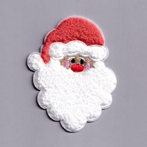 Könnte beinhalten: Gestickter Weihnachtsmann-Aufnäher mit roter Mütze und flauschigem weißem Bart. Das Gesicht des Weihnachtsmanns hat eine rosige Nase und Wangen mit einem neutralen Hautton. Der Aufnäher hat einen gewellten Rand und ist vor grauem Hintergrund platziert.