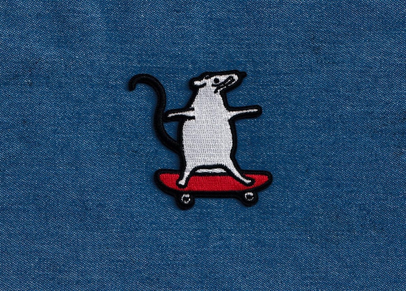 May include: Embroidered patch featuring a white rat skateboarding on a red skateboard. The rat has a black tail and is outlined in black. The patch is on a blue denim background.