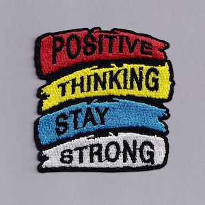 May include: An embroidered patch featuring four horizontal brushstroke shapes in red, yellow, blue, and white. The black text reads POSITIVE on the red, THINKING on the yellow, STAY on the blue, and STRONG on the white background with a black border.