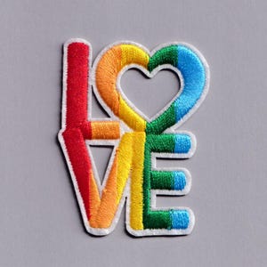 Peut inclure: Écusson brodé avec le mot "LOVE" en couleurs arc-en-ciel. Le "O" est en forme de cœur. Le patch a une bordure blanche et est posé sur un fond gris. Les couleurs comprennent le rouge, l'orange, le jaune, le vert et le bleu.