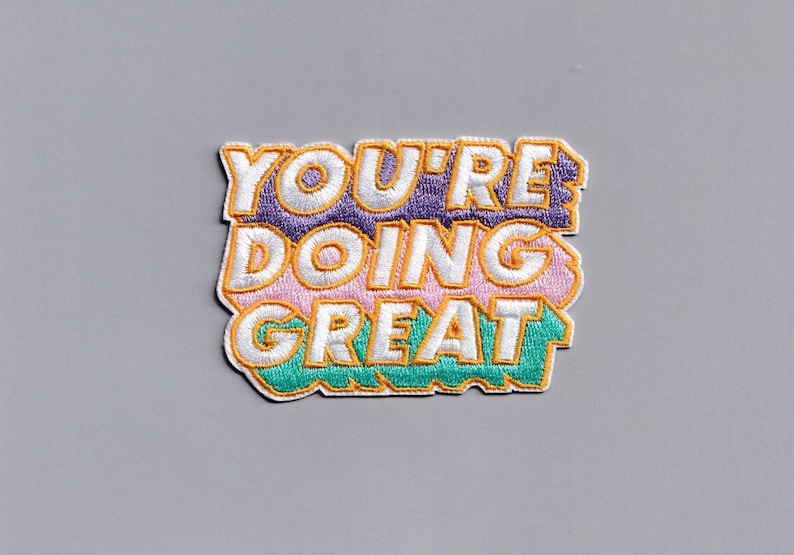 May include: A colorful embroidered patch with the text "YOU'RE DOING GREAT" in white letters with a yellow outline. The letters are layered on top of each other with different colored backgrounds.