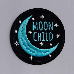 May include: Circular black embroidered patch featuring a turquoise crescent moon and white stars. The words "MOON CHILD" are embroidered in white. Suitable for clothing or accessories.